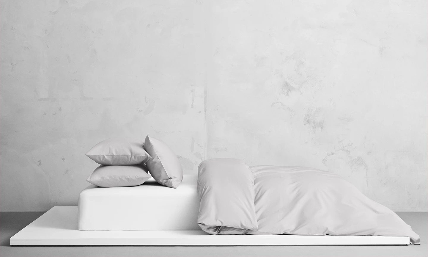 Uppbäddad säng i Naked Percale Mist Grey. Påslakan och örngott i percale av 100 % ekologisk bomull med 250 trådtäthet. Lätt och krispig känsla.