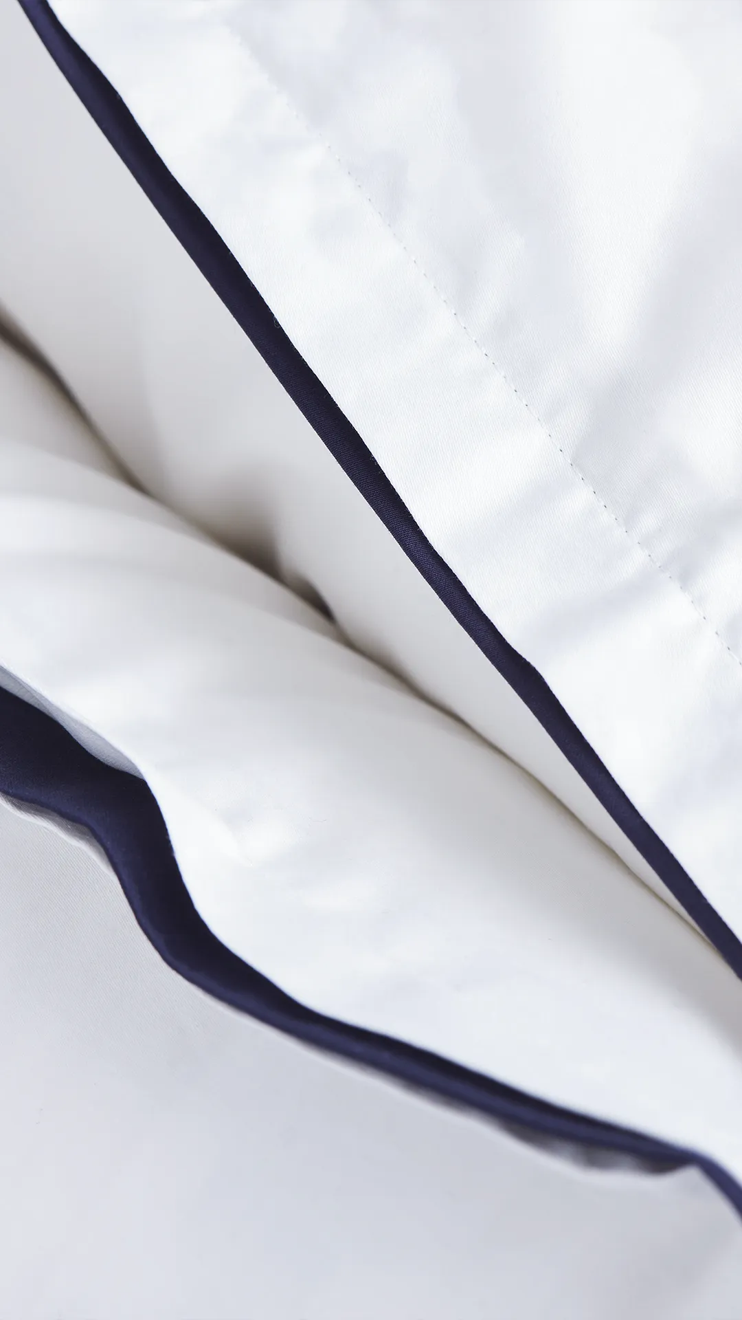 Detalj av Barton påslakan Ogland White/Navy i satin. Vit bas med navyblå kontrastkant.